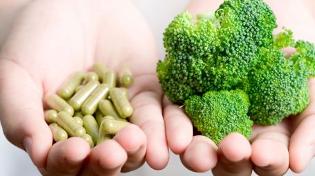 in una mano ci sono capsule vitaminiche, nell'altra i broccoli