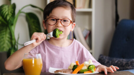 bambino felice che mangia verdure, broccoli, cavolo