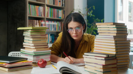ragazza studia sommersa da libri in biblioteca