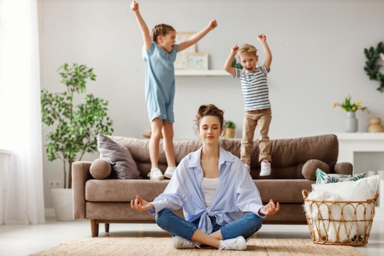 Donna fa yoga sorridendo mentre due bambini si scatenano e saltano sul divano