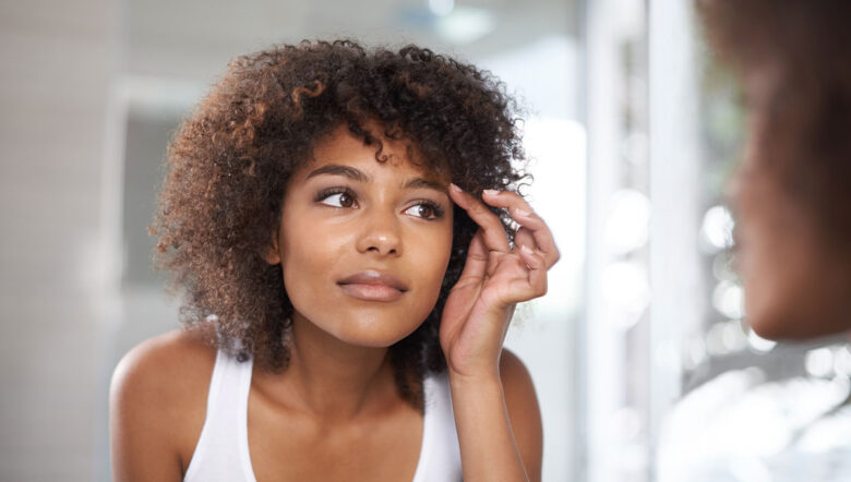 Ragazza si guarda allo specchio toccandosi all'altezza delle sopracciglia