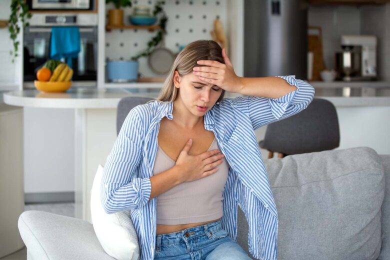 Una ragazza seduta sul divano si porta una mano al cuore e una sulla fronte