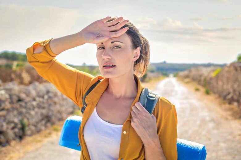 Donna si porta la mano alla fronte mentre, sotto il sole, affronta una camminata con zaino in spalla