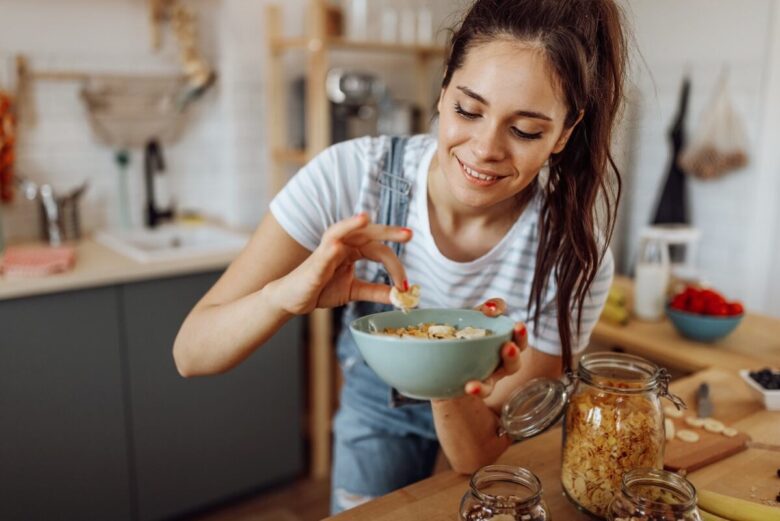 Ragazza in cucina che mette una fettina di banana in una macedonia con cereali