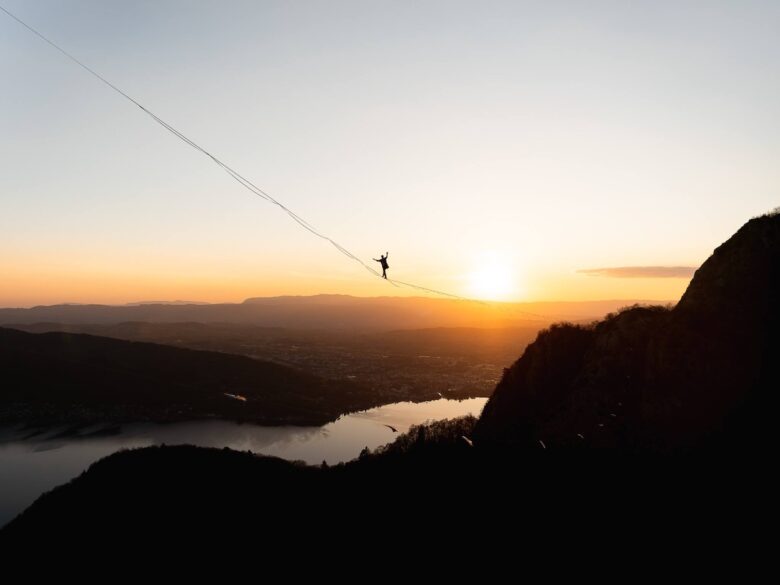 Con lo sfondo di un tramonto, una persona cammina su un filo, in montagna
