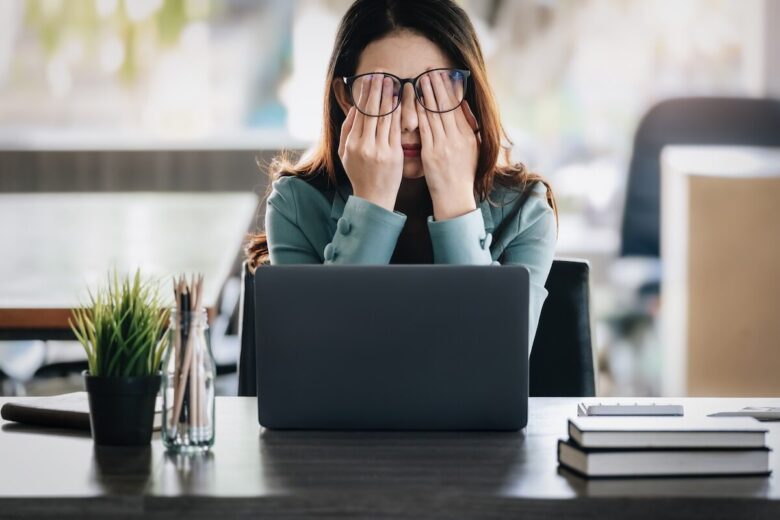 Giovame donna davanti a un computer si porta le mani sugli occhi