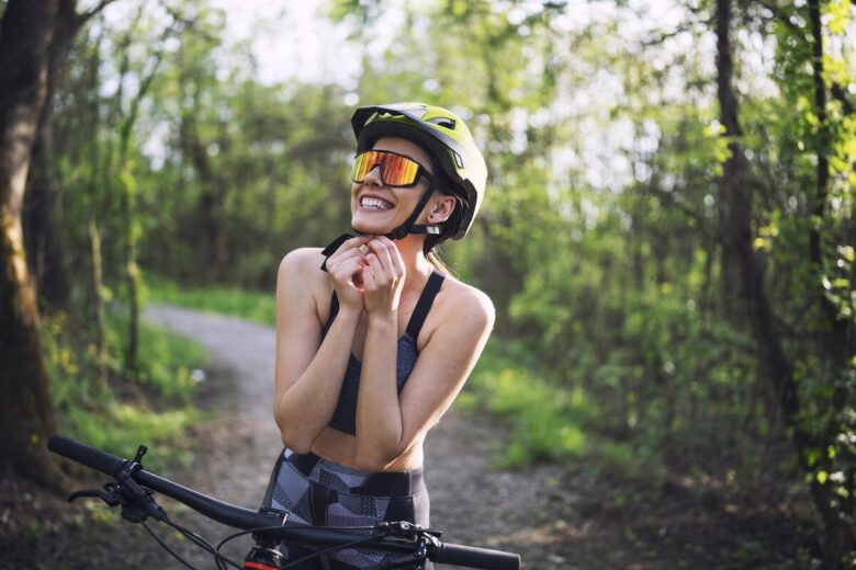 Ragazza sorridente in un bosco si allaccia il casco della bicicletta