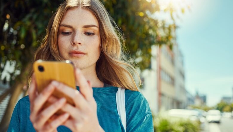 Ragazza bionda guarda lo schermo del telefonino giallo