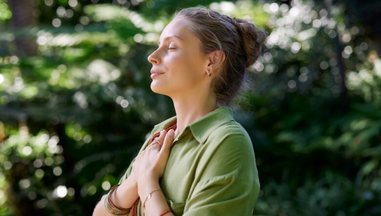 Donna nel verde che respira con gli occhi chiusi e le mani al petto