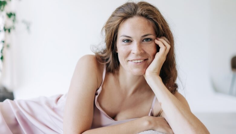 Donna sui 50 sorride sdraiata sul letto