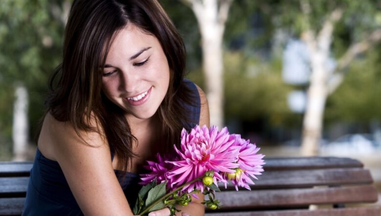Ragazza seduta su una panchina con fiore fucsia in mano guarda in basso
