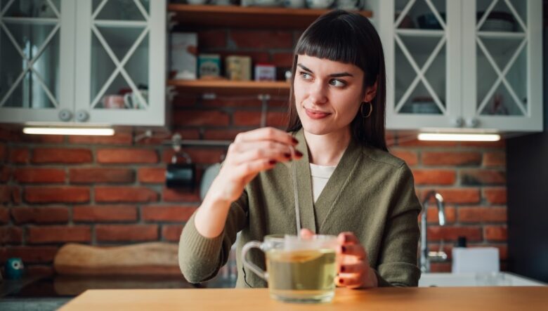 Ragazza mora in una cucina, seduta al tavolo, si prepara una tisana