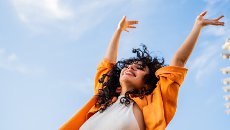 Donna felice e libera che solleva le braccia verso il cielo